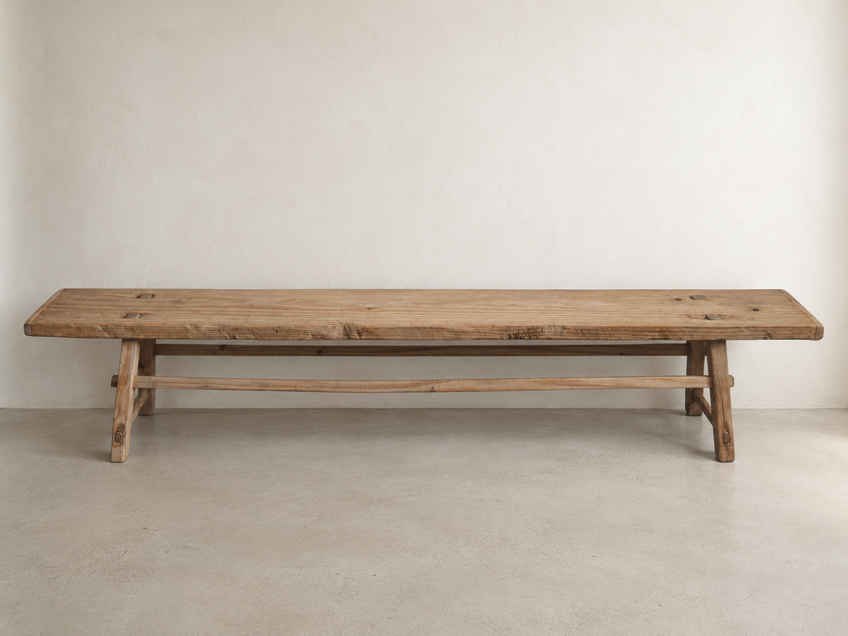 The Longhouse Bench with an elongated solid wood seat, angled legs, and connecting stretcher.