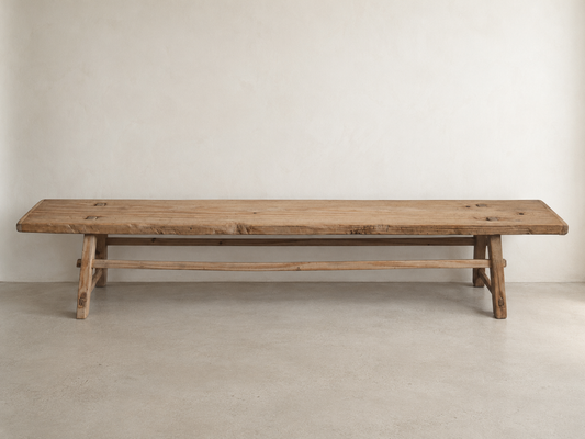 The Longhouse Bench with an elongated solid wood seat, angled legs, and connecting stretcher.
