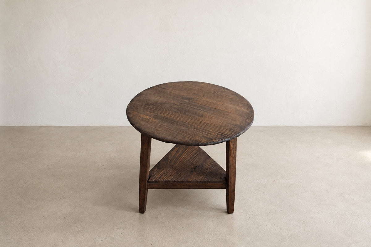 Elevated front view of The Cricket Table showing the round solid wood top and triangular lower shelf