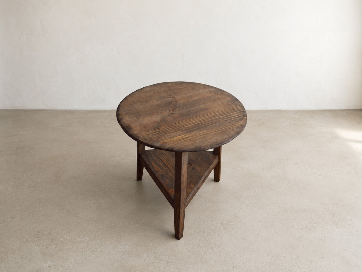 Top-angle view of The Cricket Table showing the round wood surface, natural grain, and dark aged finish