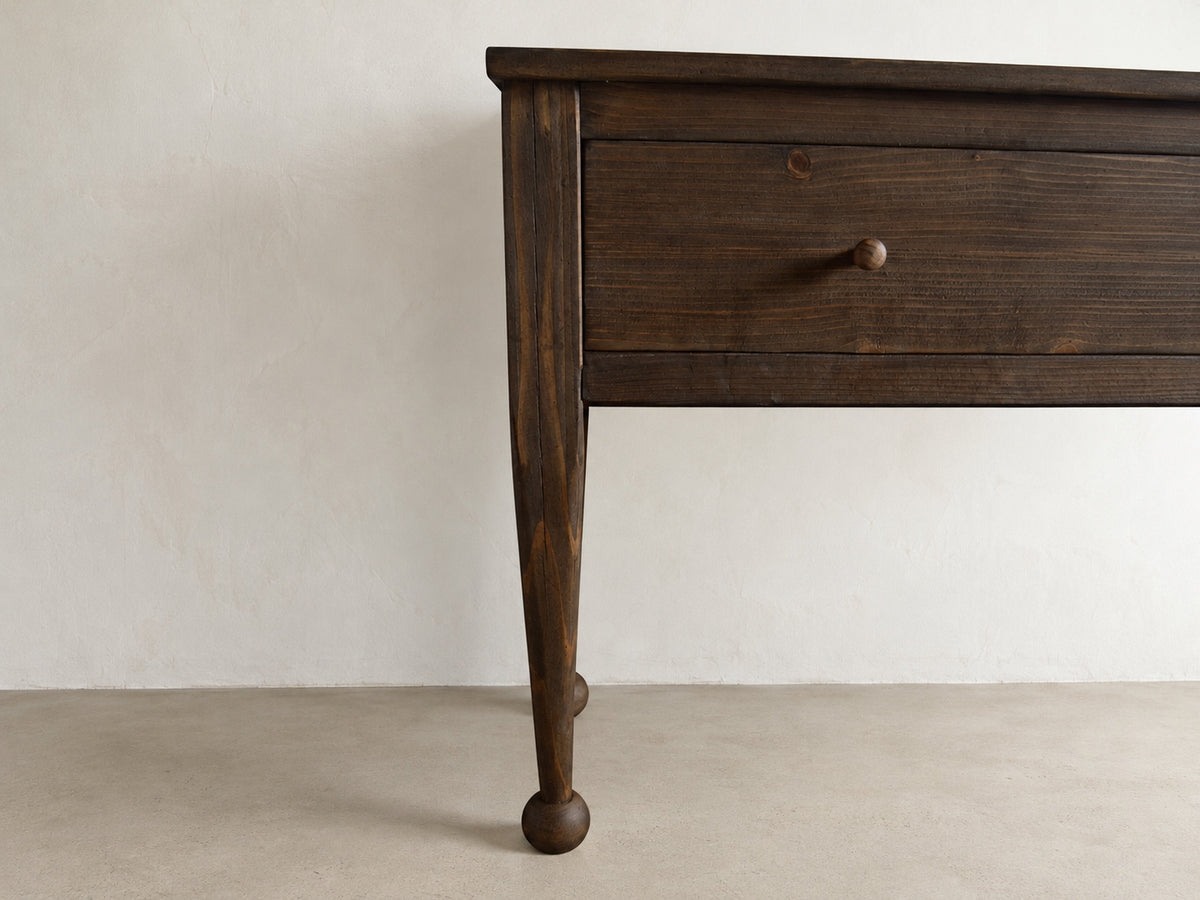 The Estate Console in Aged Umber finish, close-up of drawer, wood grain, tapered leg, and rounded foot